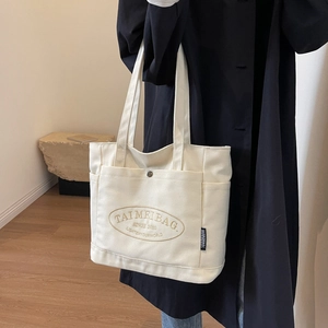 Detail shot of white canvas tote bag with front snap pocket and printed logo emblem