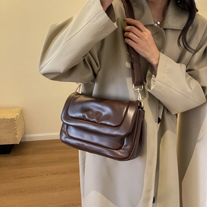 Detail of a puffy dark brown leather shoulder bag with gold buckles on a beige trench coat