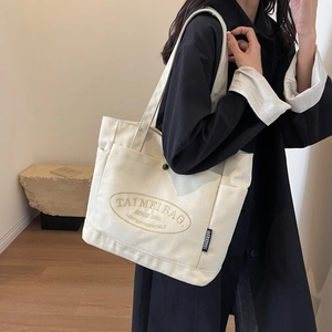 Detail of white canvas tote bag with black TAIMEI printed lettering and woven side label