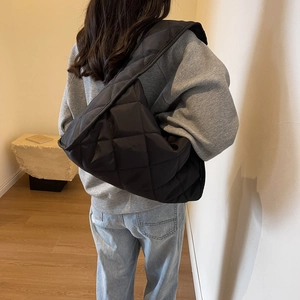 Back view of a large black quilted puffer shoulder bag worn by a model in a minimalist room