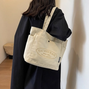 Detailed back view of off-white canvas tote bag with embroidered logo on a shoulder
