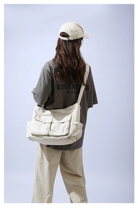 Model wearing large off-white canvas crossbody bag with dual front utility pockets