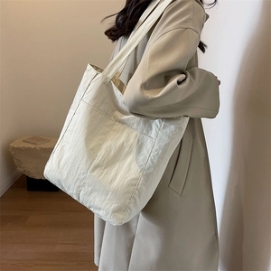 Detail of minimalist beige nylon tote bag showing lightweight texture on a model's shoulder