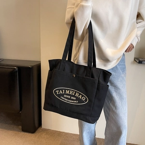 Close-up of black canvas tote bag with embroidered logo and front pocket detail
