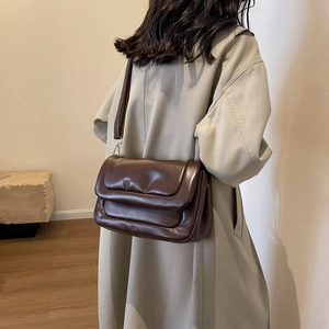 Detail of dark brown quilted crossbody bag shown on model with aesthetic beige coat