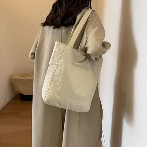 Detail of minimalist beige fabric tote bag with front pocket worn with khaki trench coat