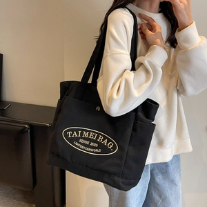 Close-up of black canvas tote bag with oval logo embroidery worn on model shoulder