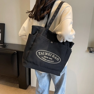 Detailed view of black canvas tote bag with side pocket shown on shoulder