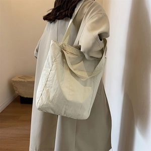 Minimalist cream nylon tote bag with shoulder strap shown in a modern interior setting