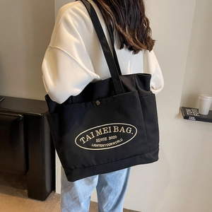 Detail showing high-capacity black canvas tote bag with front snap pocket and embroidery