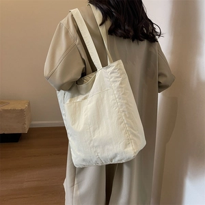 Close-up of minimalist beige canvas tote bag with large front pocket on shoulder