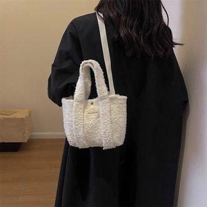 Détail du mini cabas blanc en fausse fourrure avec logo sur fond de manteau noir élégant