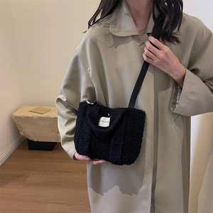 Gros plan d'un sac bandoulière en polaire noire avec étiquette tissée sur un mannequin