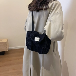 Modèle portant un sac cabas en peluche noire avec étiquette logo blanche sur manteau gris