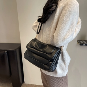 Detail of a black quilted puffer shoulder bag with gold metal hardware and a sleek PU finish