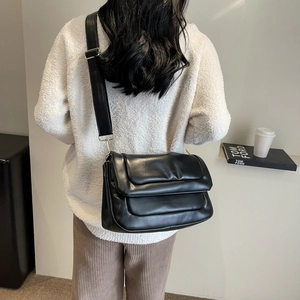 Detail of black puffer crossbody bag with quilted texture and wide adjustable shoulder strap