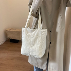 Minimalist beige tote bag in nylon fabric with large front pocket and long shoulder straps