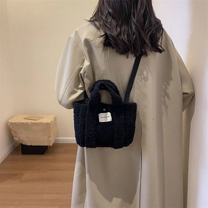Détail d'un mini sac cabas en peluche noire avec écusson logo blanc et bandoulière longue