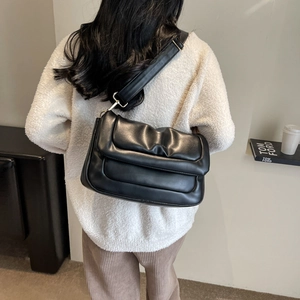 Detail of a black quilted shoulder bag with soft pleated texture and wide strap