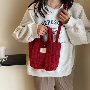 Détail du sac bandoulière rouge en polaire teddy avec étiquette blanche porté par le mannequin