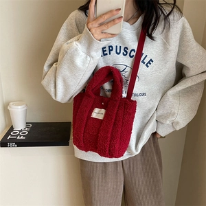 Détail d'un sac à bandoulière en peluche rouge avec étiquette blanche et sangle