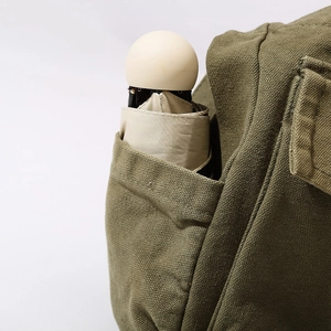 Army green canvas shoulder bag with a side pocket holding a compact beige umbrella