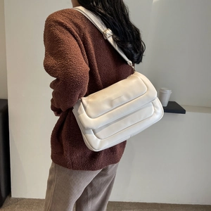Detail of a quilted cream puff shoulder bag featuring metallic logo and golden hardware