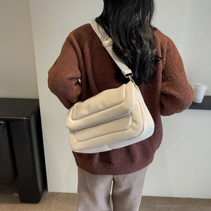 Quilted beige puffer shoulder bag detail with wide strap worn over a brown sweater