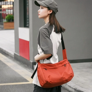 Large orange-red nylon messenger bag with black wide strap shown on a street model