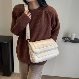 Detail of cream quilted crossbody bag with adjustable wide strap shown on a model