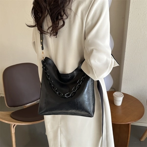 Fashionable black PU leather shoulder bag with bold chain detail shown on a model