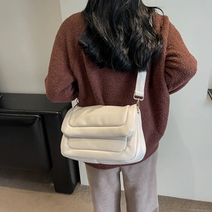 Close-up of cream quilted puffer bag with horizontal stitching and wide shoulder strap