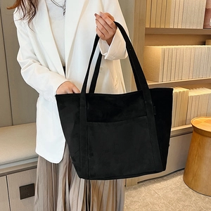 Close-up of a black matte PU tote bag on a white blazer during a lifestyle shoot