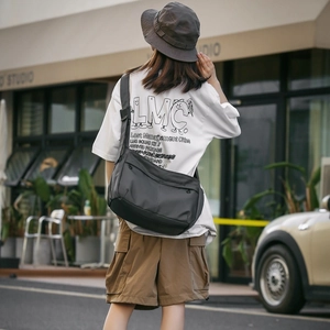 Detail of grey nylon messenger bag with multiple zippers and adjustable strap on a model