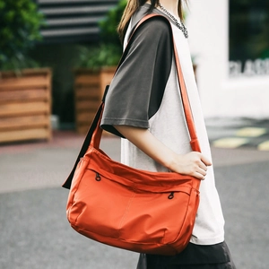 Close-up of bright orange nylon crossbody bag with wide shoulder strap and front zip pocket