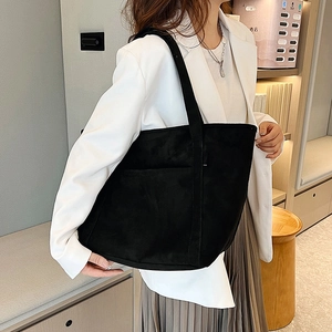 Detail showing the minimalist black suede tote bag with practical open front pocket