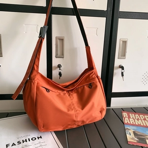 Close-up of orange nylon shoulder bag with zipper pockets on a silver metal bench