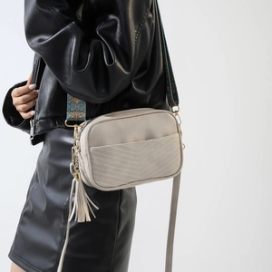 Detail of cream PU crossbody bag with bohemian strap and fringe on black outfit
