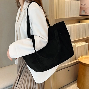 Detail of a large black canvas tote bag showing the textured fabric and functional side pocket