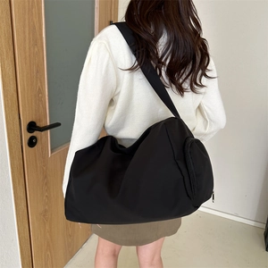 Rear view of a black oxford cloth crossbody bag showing capacity and fit on female model