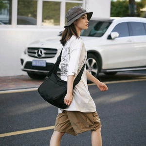 Detail of a large black nylon messenger bag with side pockets during a street walk