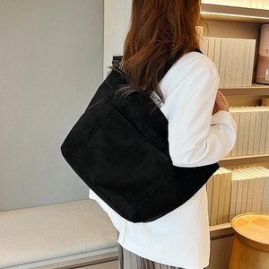 Side view of a large black canvas tote bag worn by a model in a cozy library setting
