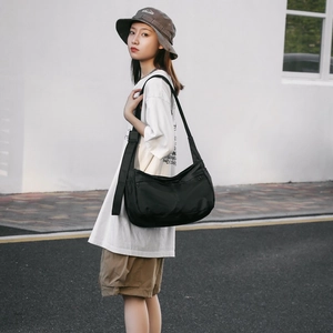 Detail of black nylon crescent shoulder bag featuring dual front zipper pockets on model