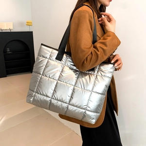 Detail of silver quilted puffer tote bag with metallic texture and black shoulder strap