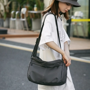 Detail view of dark grey nylon crossbody bag with white stitching on a model in street setting
