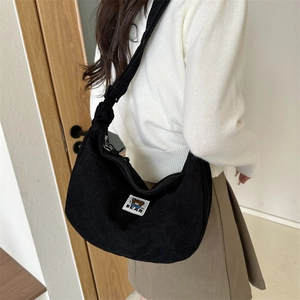 Detail of black corduroy crescent bag with bear patch worn by a model in a cozy setting