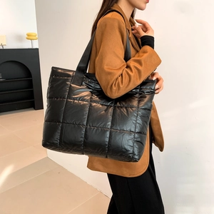 Detail of a large black quilted tote bag with glossy finish and wide textile shoulder strap