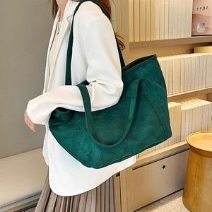 Close-up of a large dark green faux suede tote bag on a model wearing a white suit