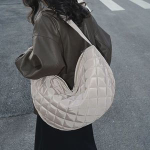 Vue détaillée du sac croissant en nylon matelassé beige porté par un mannequin en ville