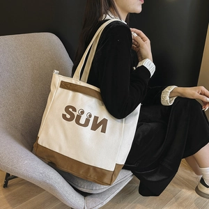 Detail of canvas tote bag with SUN print carried by a model sitting on a sofa